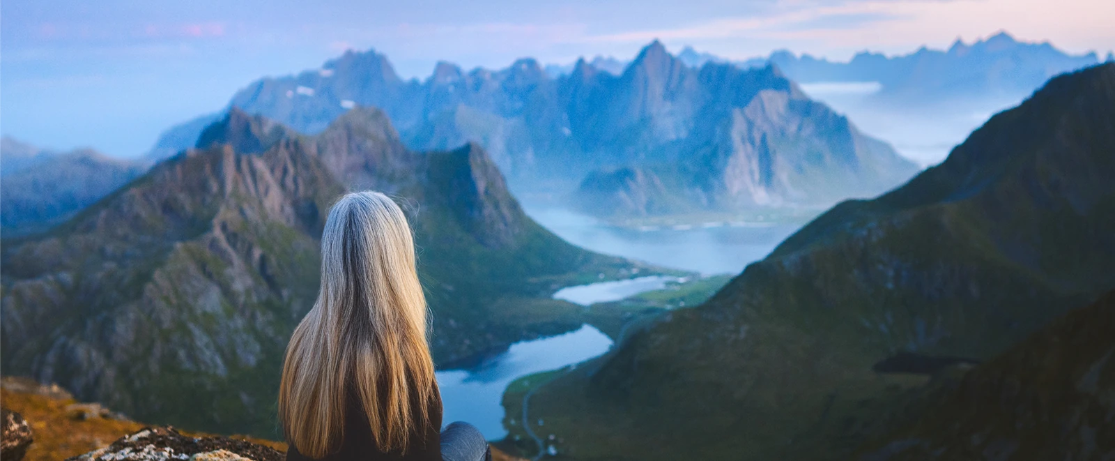 older hiker sitting on cliffside overlooking mountainscape