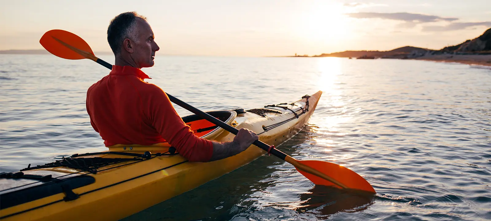 senior man kayaking during sunset