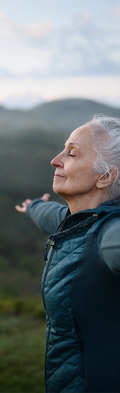 relaxed older woman in nature stretching her arms and taking in the beauty