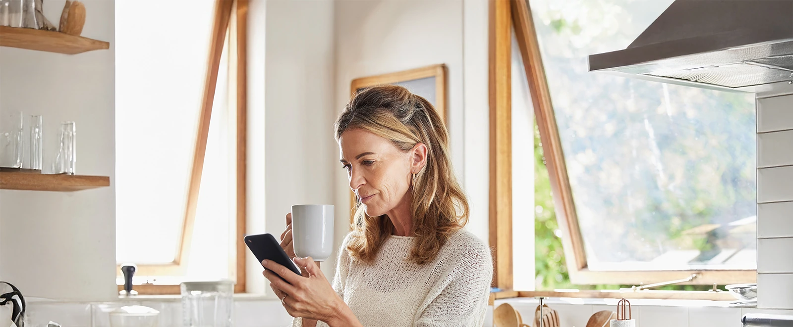 mature woman at home looking at her phone and holding coffee mug