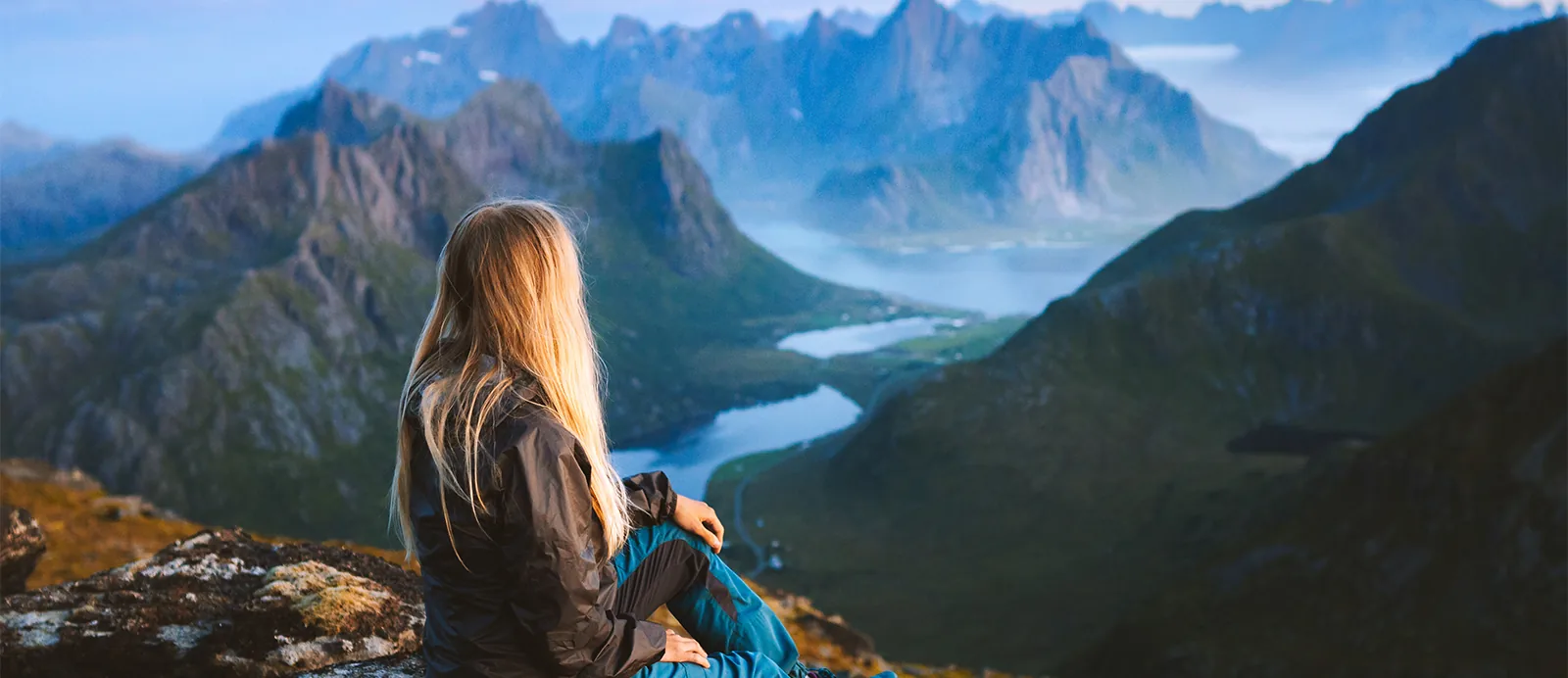 young female hiker sitting at top of mountain looking out over the valley